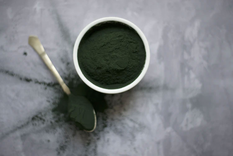 Green powder in a white bowl with a spoon set beside it