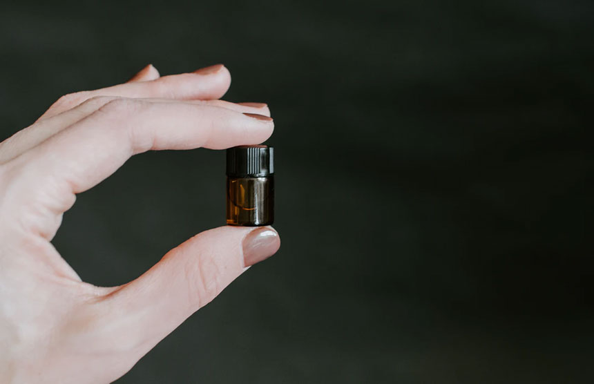 A hand holding a small amber bottle of super-concentrated kratom against a dark background