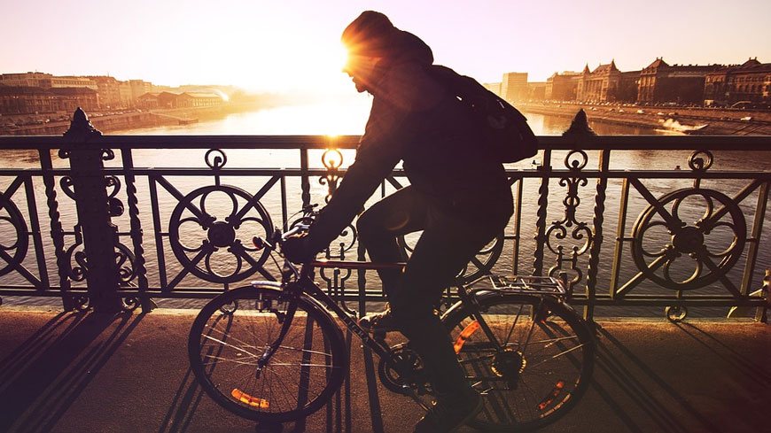 A man cycling over a bridge at sunset.