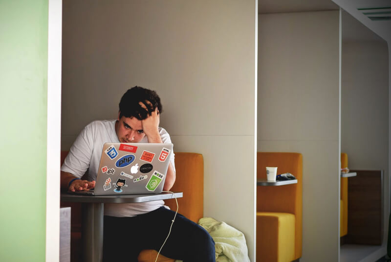 Stressed man sits at booth with laptop.