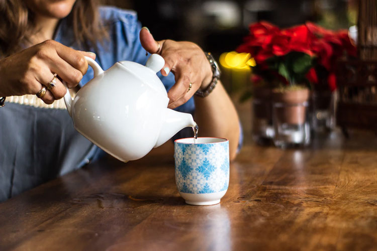 A woman pouring a clear liquid from a white teapot into a patterned mug