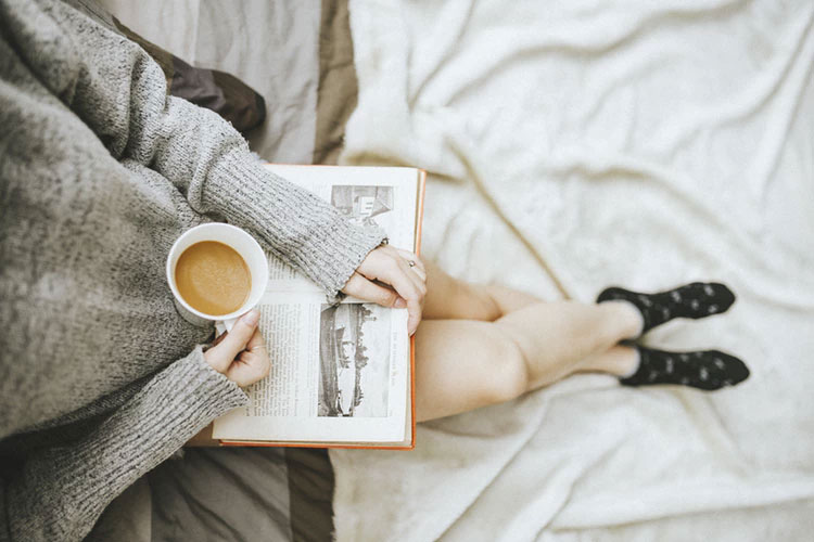 women reading book holding a cup of tea