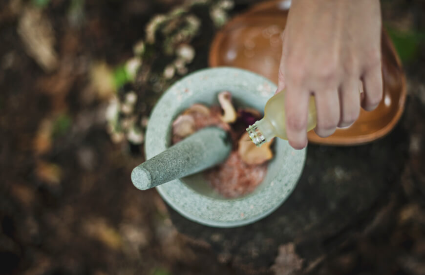 A hand gripping a small bottle over a mortar and pestle.