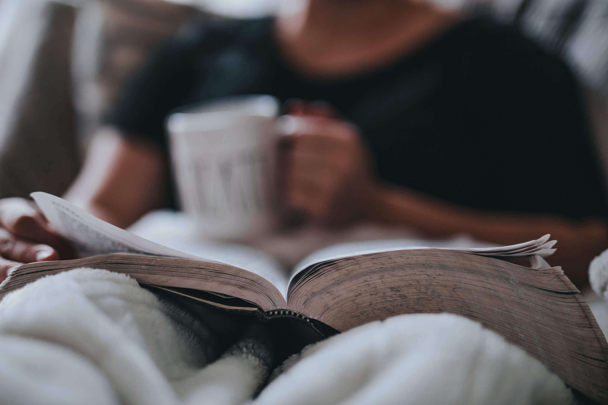 Man reads book with coffee in hand.