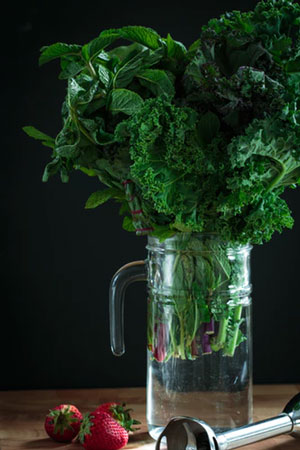 A bouquet of greens in a glass jug with strawberries sitting nearby