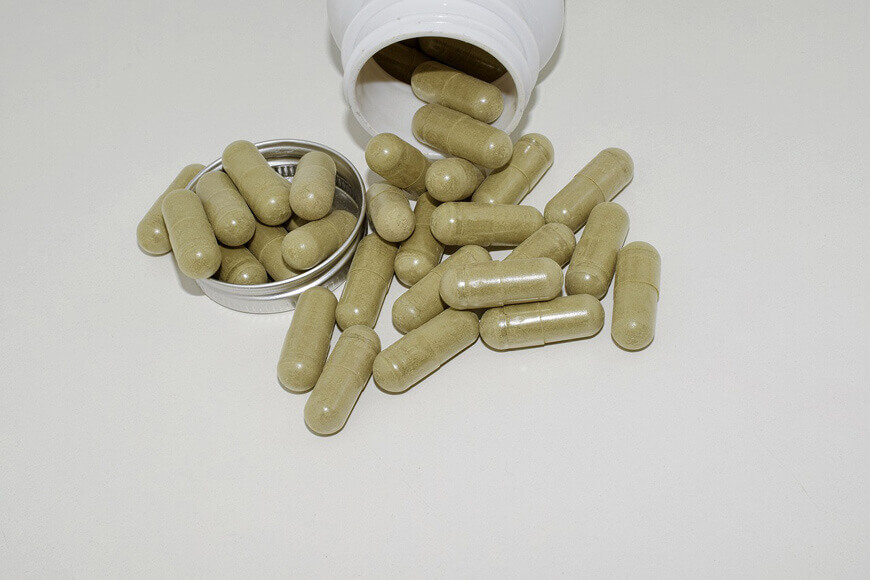 Capsules of green powder spilling out of a container