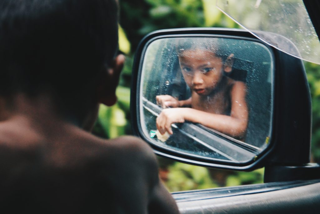  A Malaysian boy looking in the side mirror of a car in the jungle.