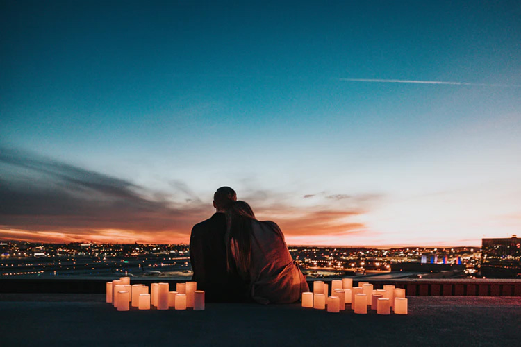 A couple surrounded by candles sits on a rooftop to watch the sunset