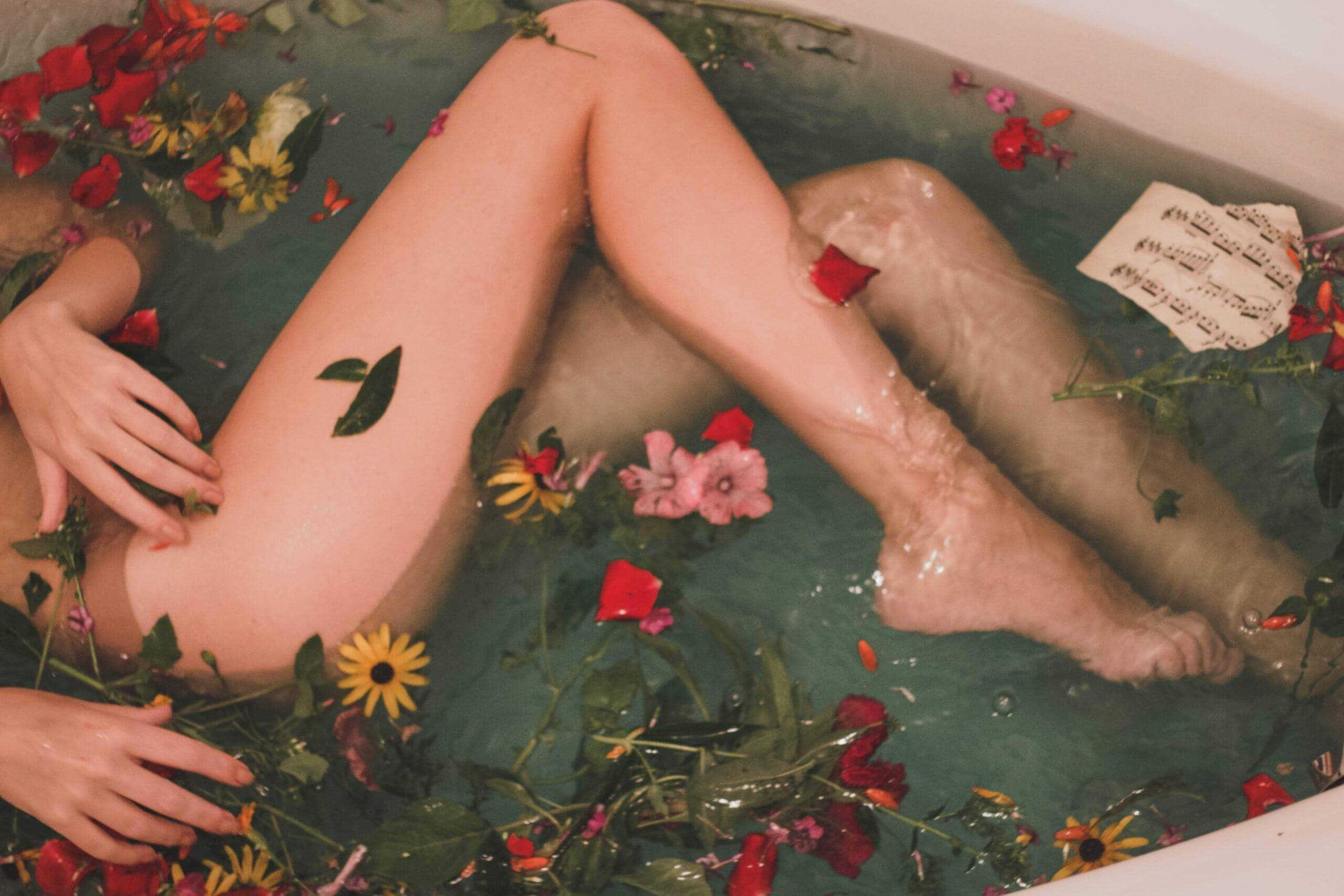 bare legs in an herbal bath with multicolored flowers