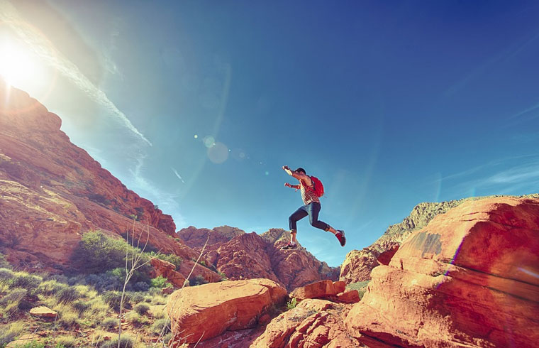 A man with a backpack leaping over rocks in the desert