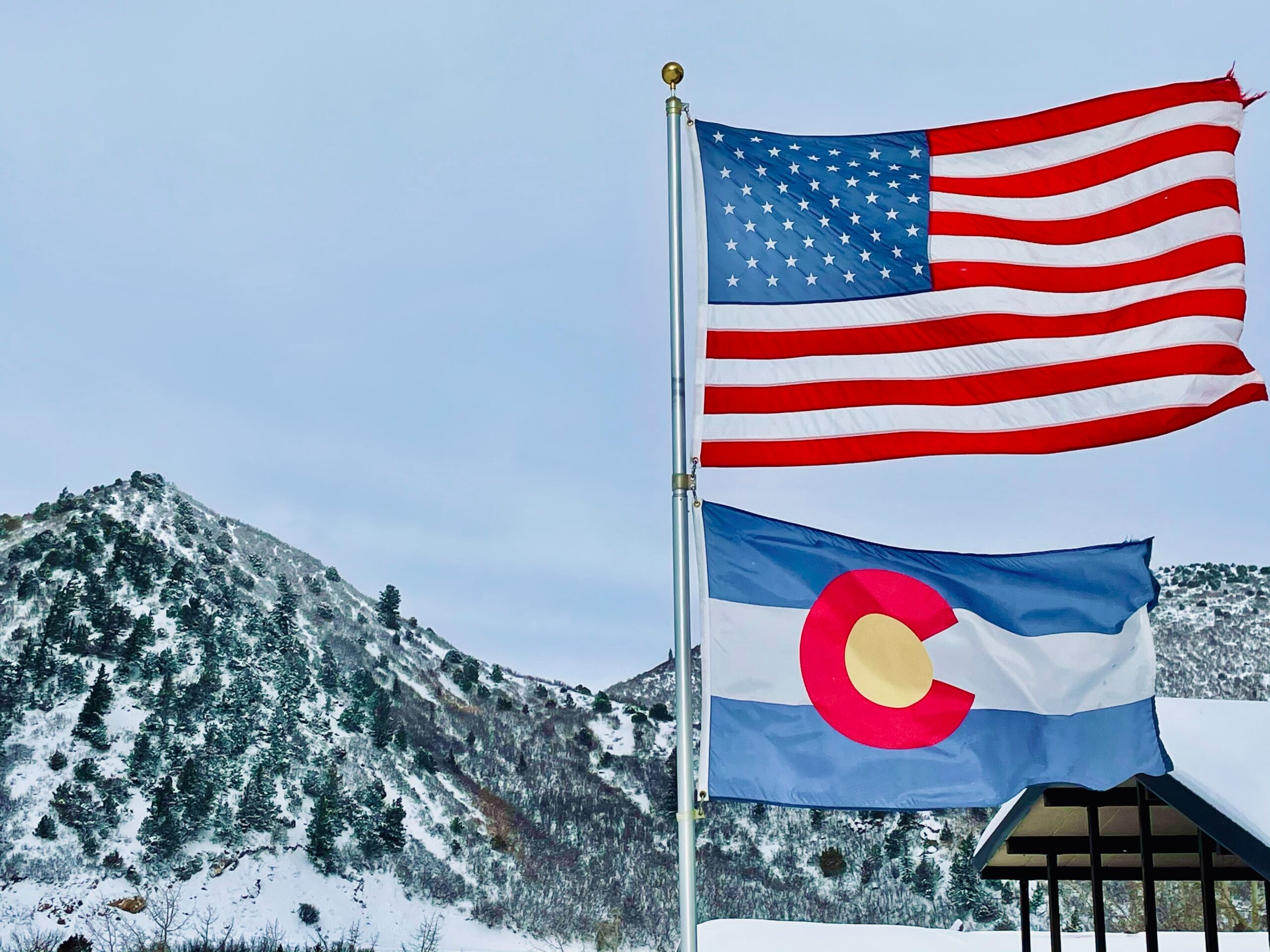U.S. flag and Colorado flag on a pole against a snowy mountain backdrop