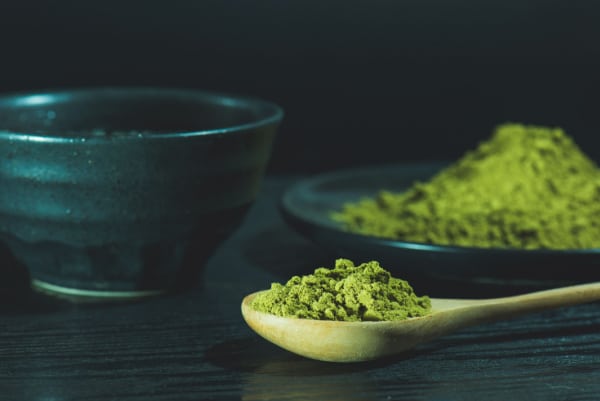 A tablespoon of kratom powder on a dark background