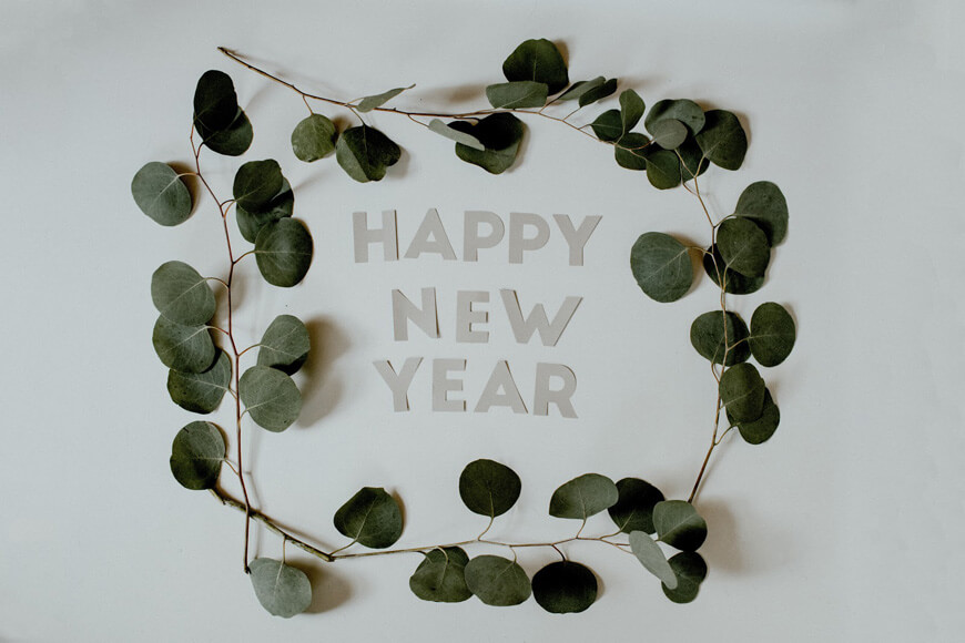 Letters spelling out happy new year surrounded by plant leaves
