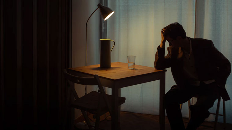 Man sits at table illuminated by a single lamp