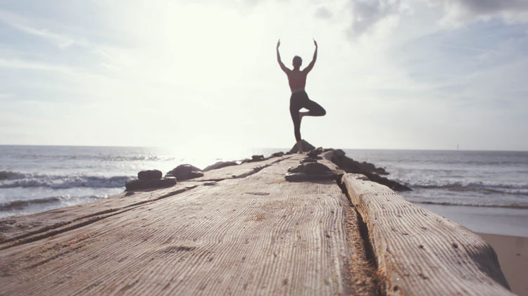 A man standing on a jetty holding in a yoga pose with his arms up to the sky
