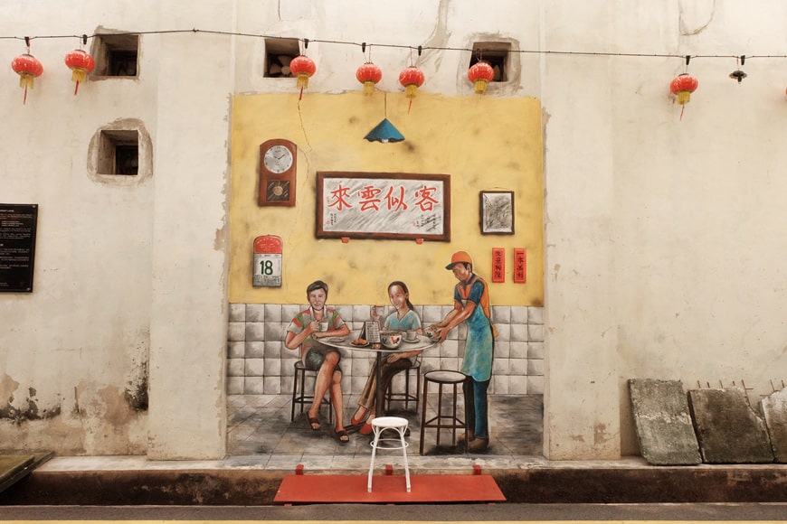 An outdoor artwork of a Malaysian couple drinking tea.