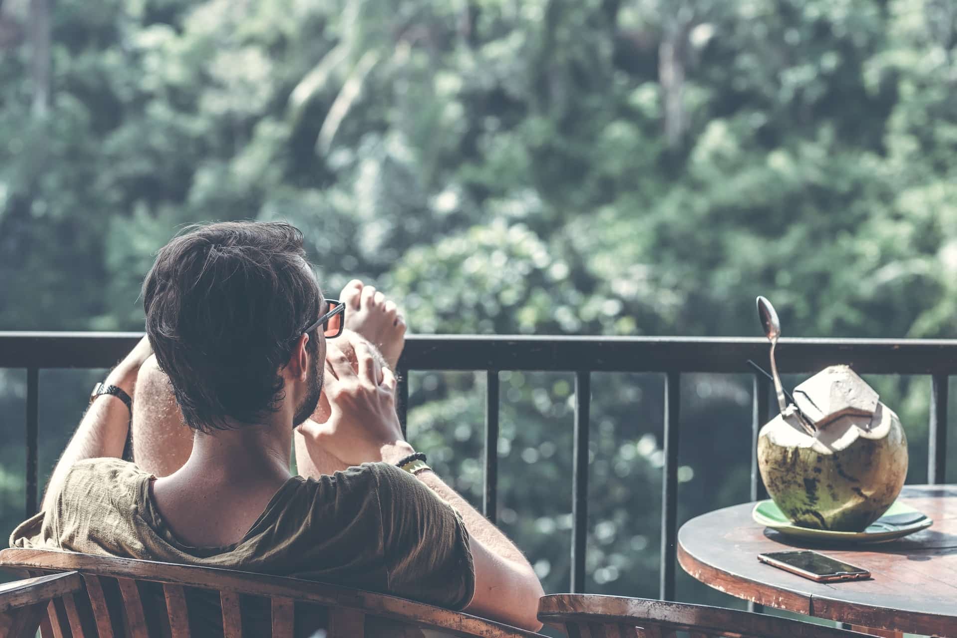 relaxed man on a balcony looking at lush green trees