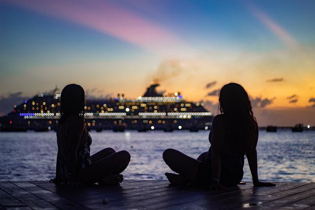 Two female silhouettes alongside ocean and cruise ship at sunset 
