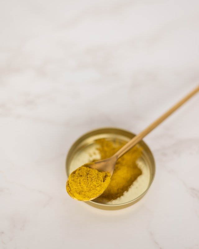 Turmeric spice in a small spoon from a gold dish