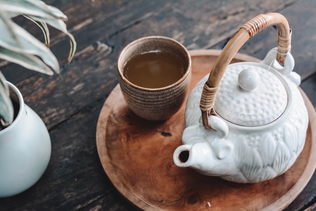 A cup of herbal tea alongside a ceramic teapot 