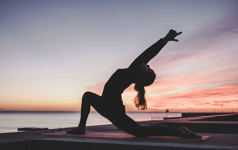 Woman does yoga as a holistic fitness practice in front of sunset